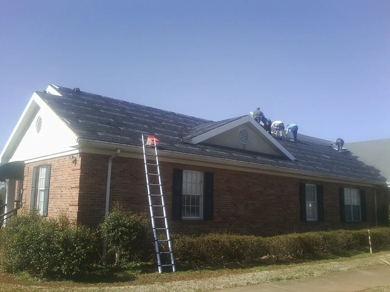 Crew tearing shingles off a brick ranch roof with a ladder set — Emergency Roof Repair work by our crew in Parlier