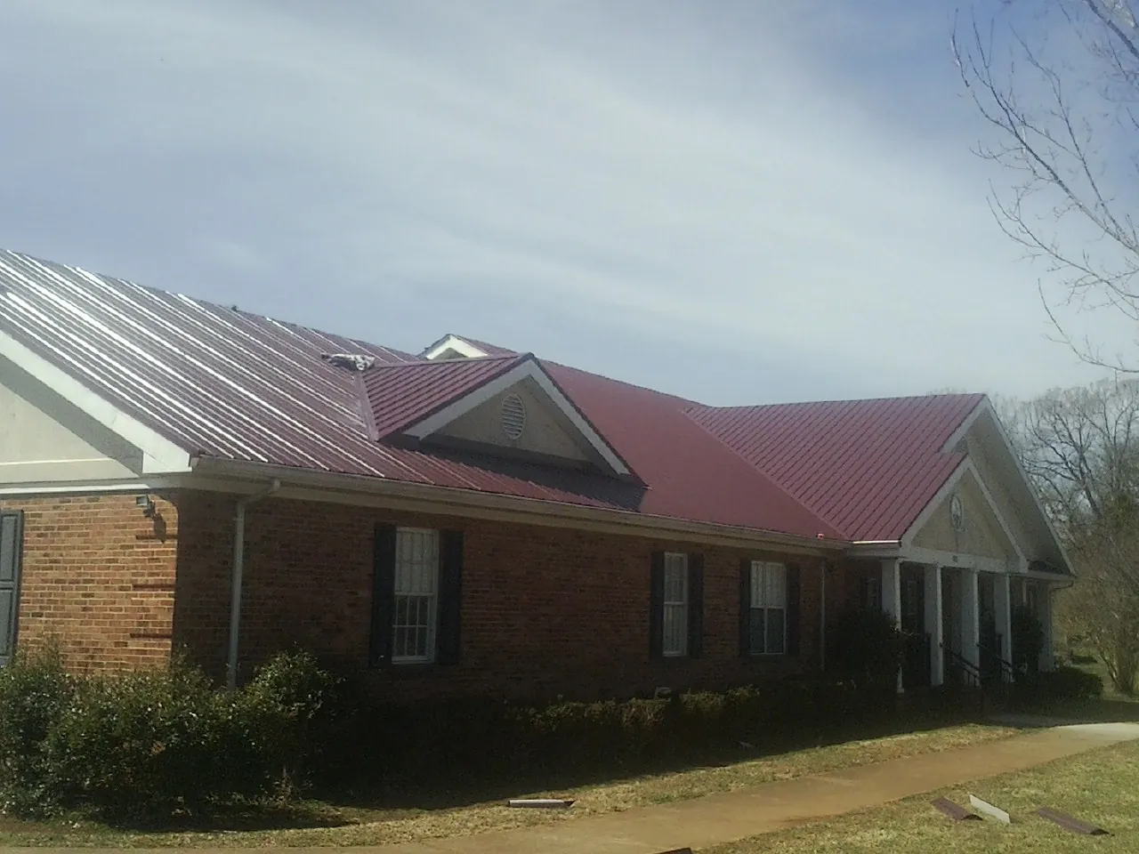 Red metal roof with gabled entries on a long brick building, from a Hail Damage Roof Repair job in Parlier