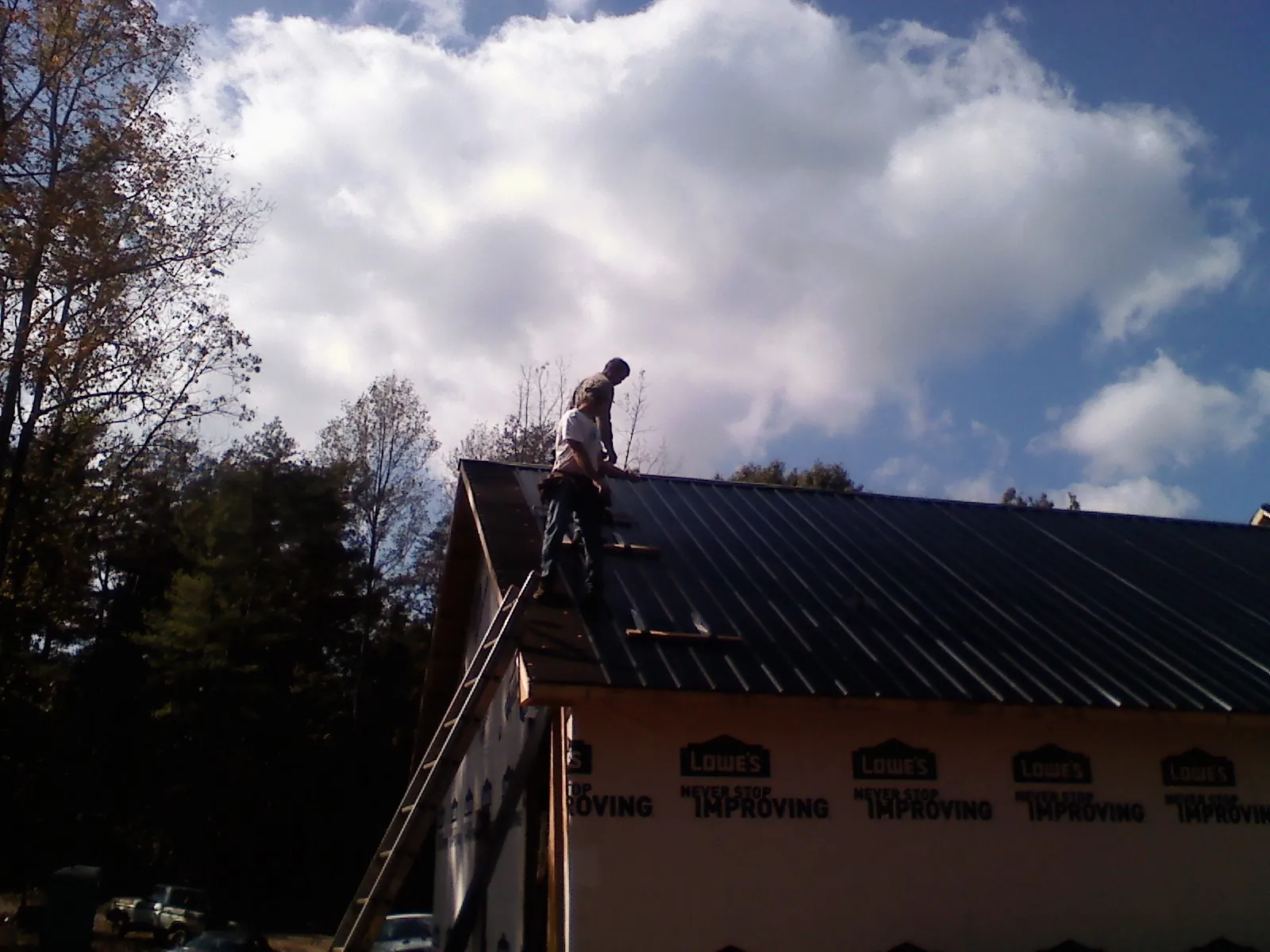 Roofer fastening dark metal panels high against a cloudy sky, from a Roof Inspection job in Parlier
